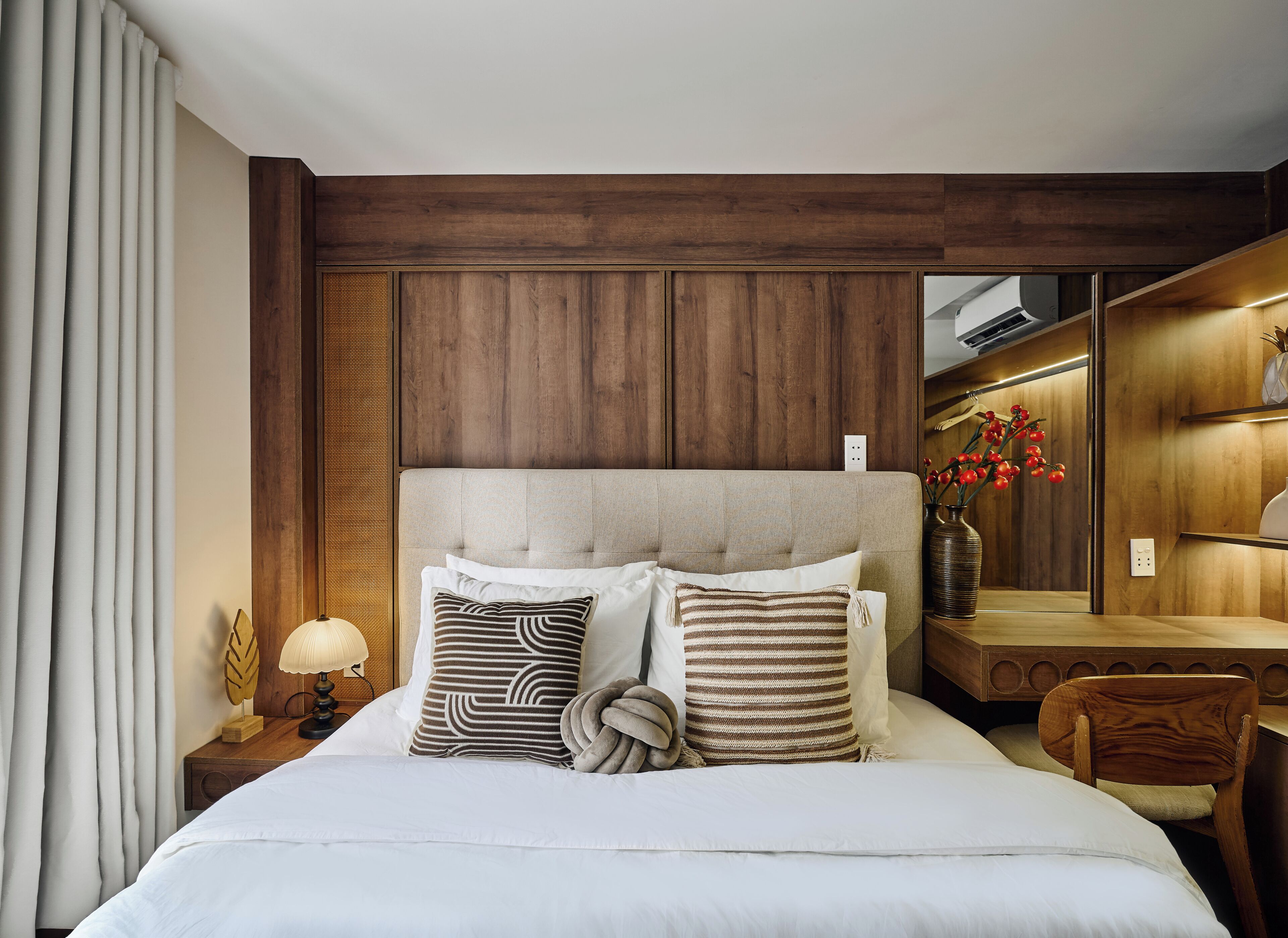 Une chambre d’hôtel avec un grand lit, une tête de lit en bois, une table de chevet avec une lampe, un miroir et un vase avec des fleurs.