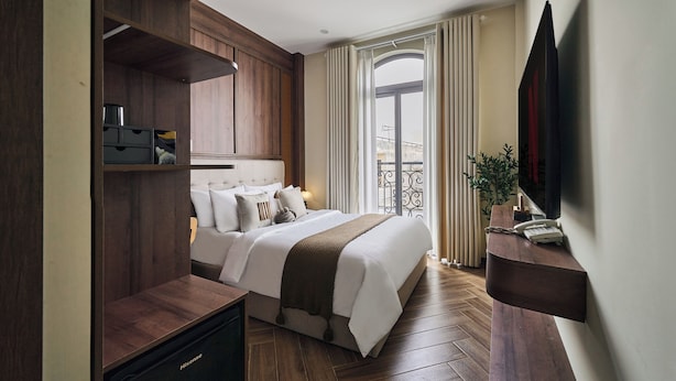 A modern hotel room with a large bed, wooden paneling, a flat-screen TV, and a balcony with curtains. - Centoria Hotel Quang Trung by Urban B (Ho Chi Minh City)