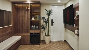 A modern hotel room with a wooden bench, a potted plant, a built-in wardrobe, a small refrigerator, and a wall-mounted phone. - Centoria Hotel Quang Trung by Urban B (Ho Chi Minh City)