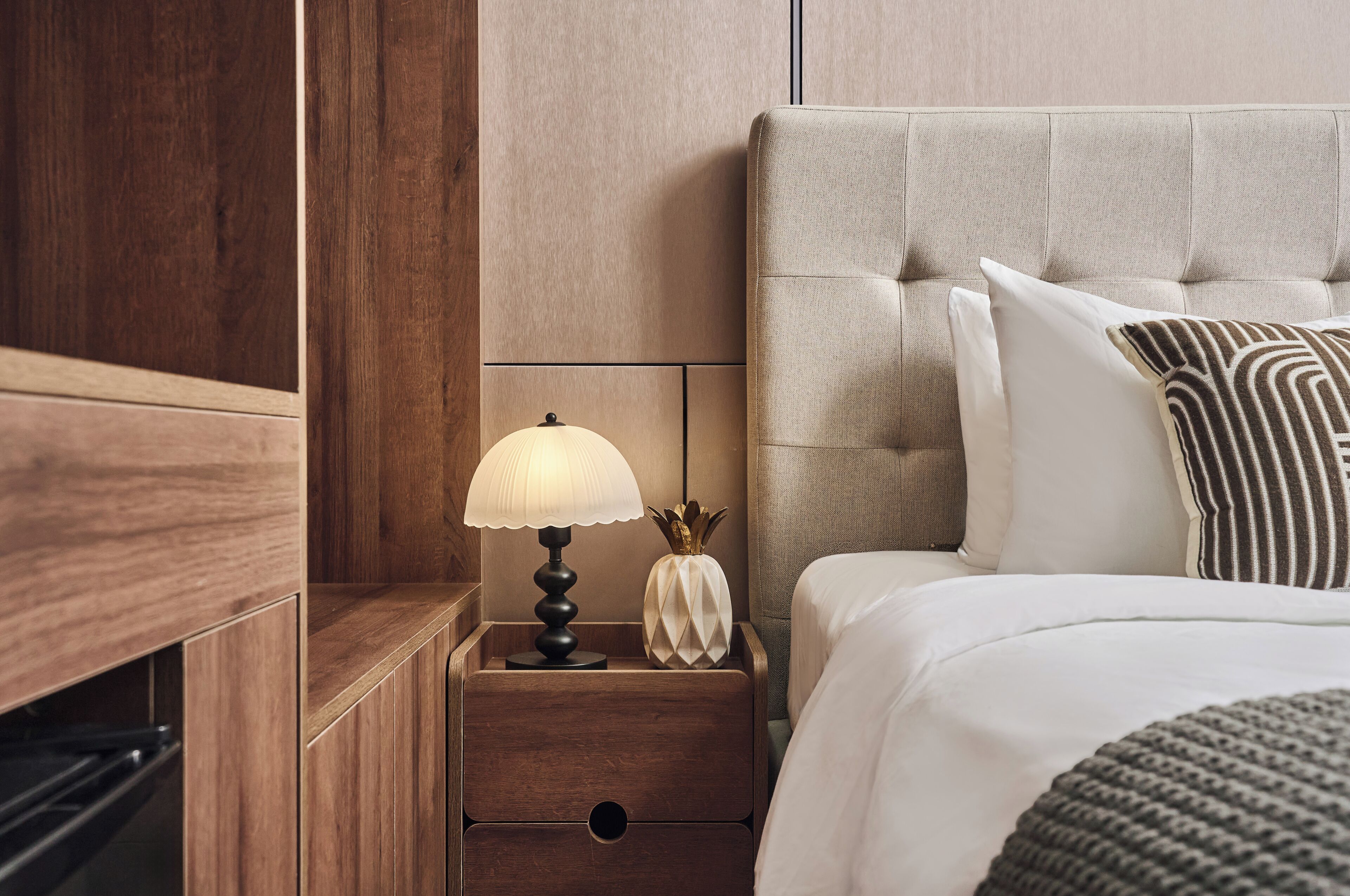 A neatly made bed with a tufted headboard, a bedside lamp, and a decorative vase.