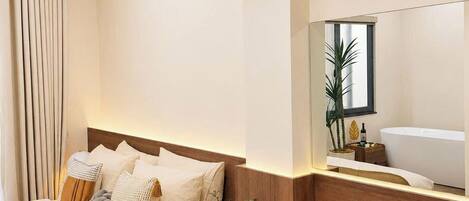 A hotel room with a bed, bedside table, and a large mirror.