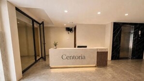 A reception desk labeled 'Centoria' with a modern design, a potted plant, a wall-mounted TV, and a glass door entrance. - Centoria Hotel Quang Trung by Urban B (Ho Chi Minh City)