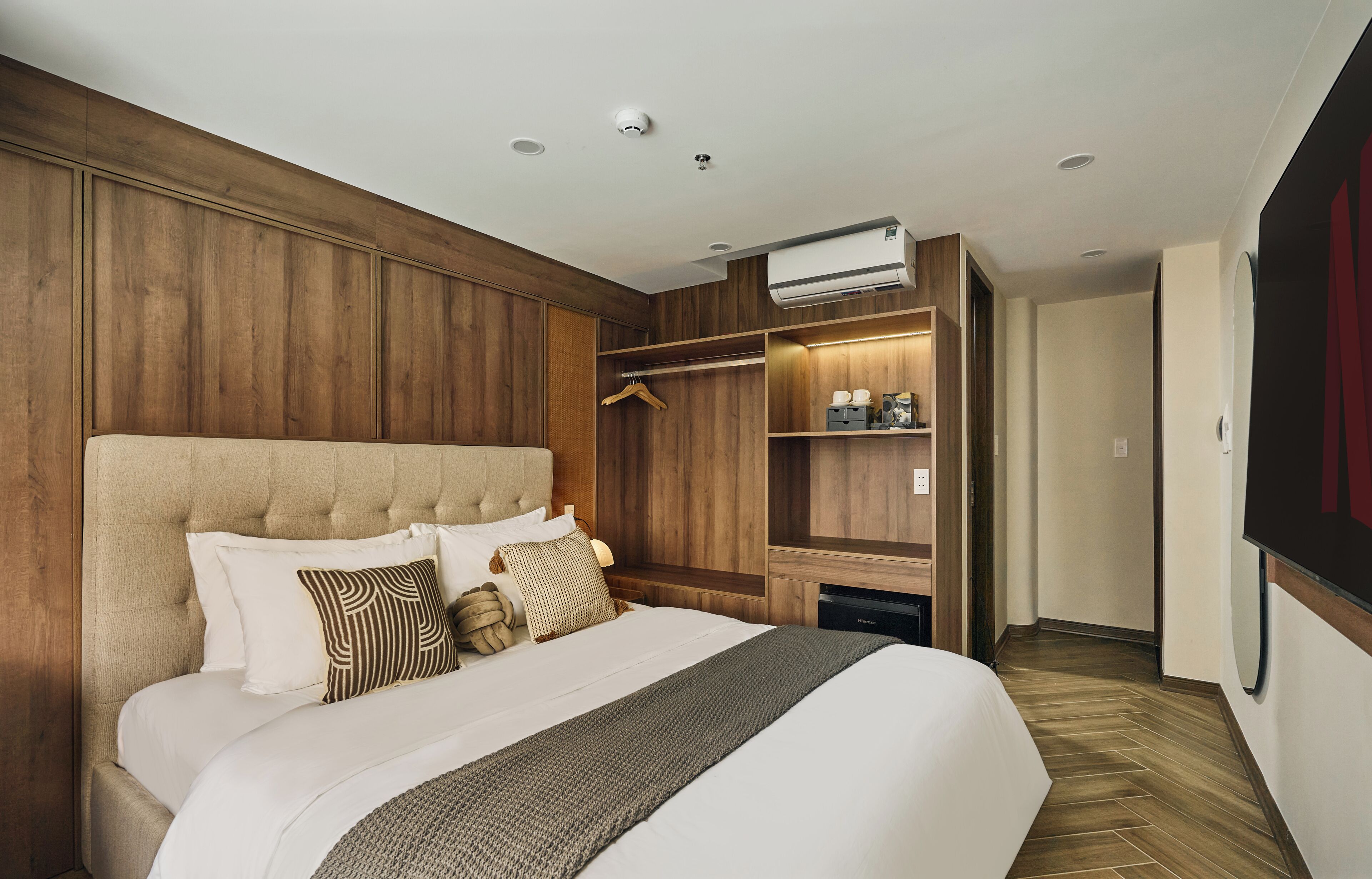 Habitación de hotel con una cama grande, paneles de madera, aire acondicionado, vestidor y televisor.