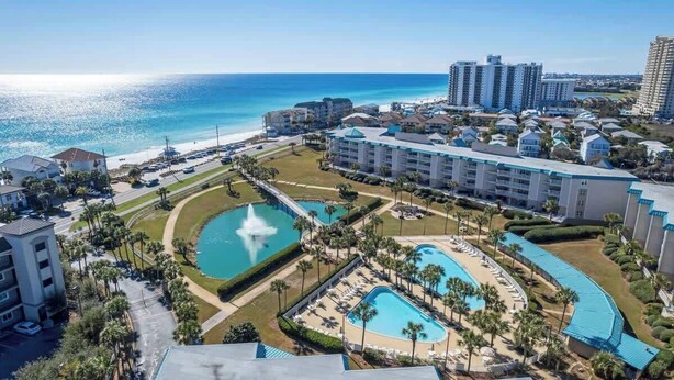 Un complejo turístico con varias piscinas, una fuente central y vistas a la playa.