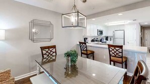 Una cocina moderna con armarios blancos, una isla central y un comedor con mesa de vidrio y sillas de madera.