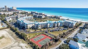 Un hotel frente al mar con varias edificaciones, una cancha de tenis y vistas a la playa.