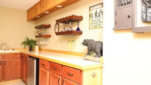 Una cocina con armarios de madera, lavavajillas, botellero y un reloj.
