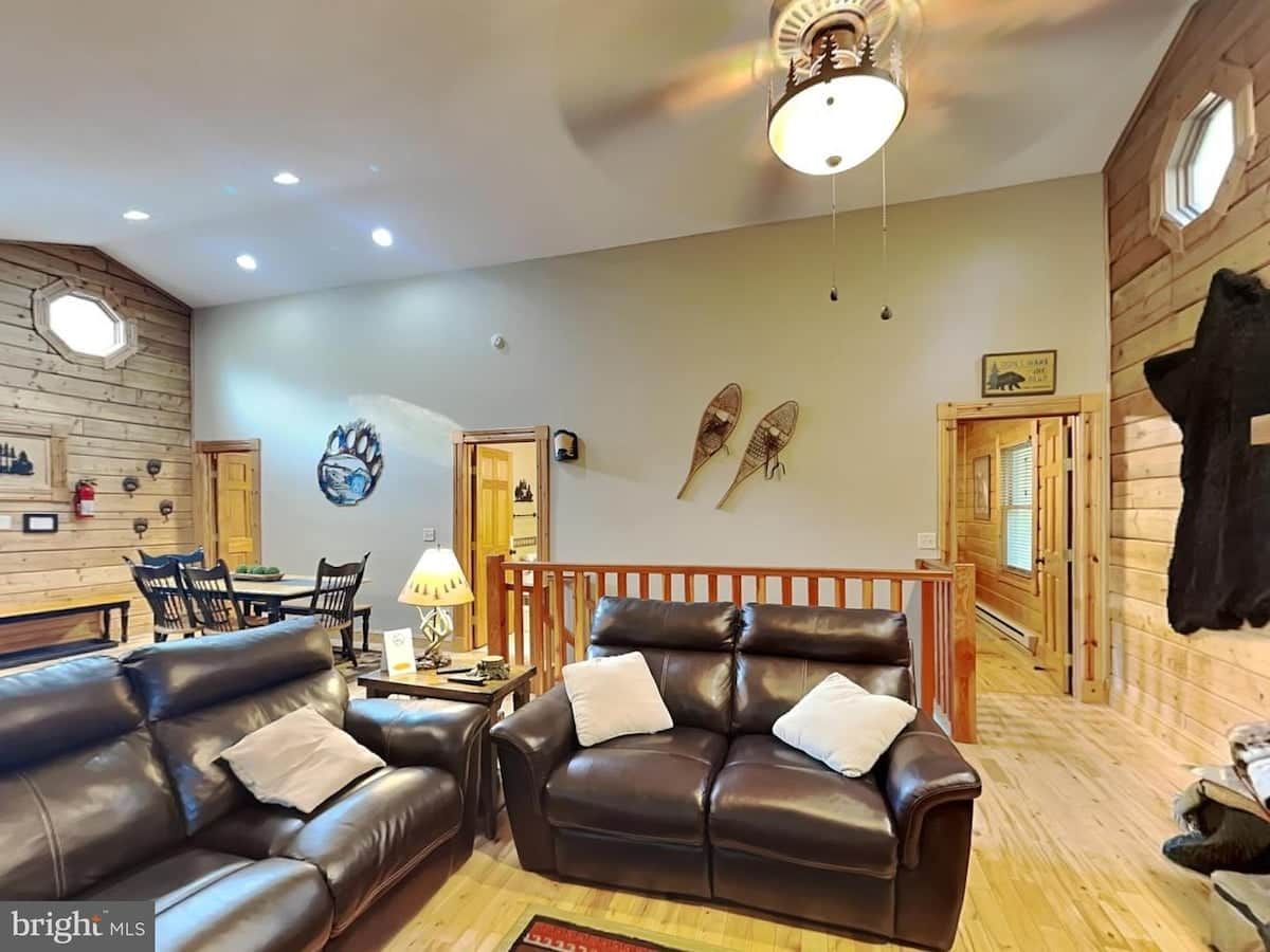 A living room with leather sofas, a dining table, and a ceiling fan.