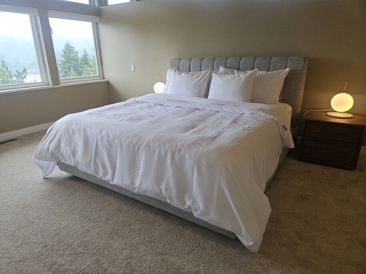 A bedroom with a bed, a nightstand, a lamp, and a window with a view.