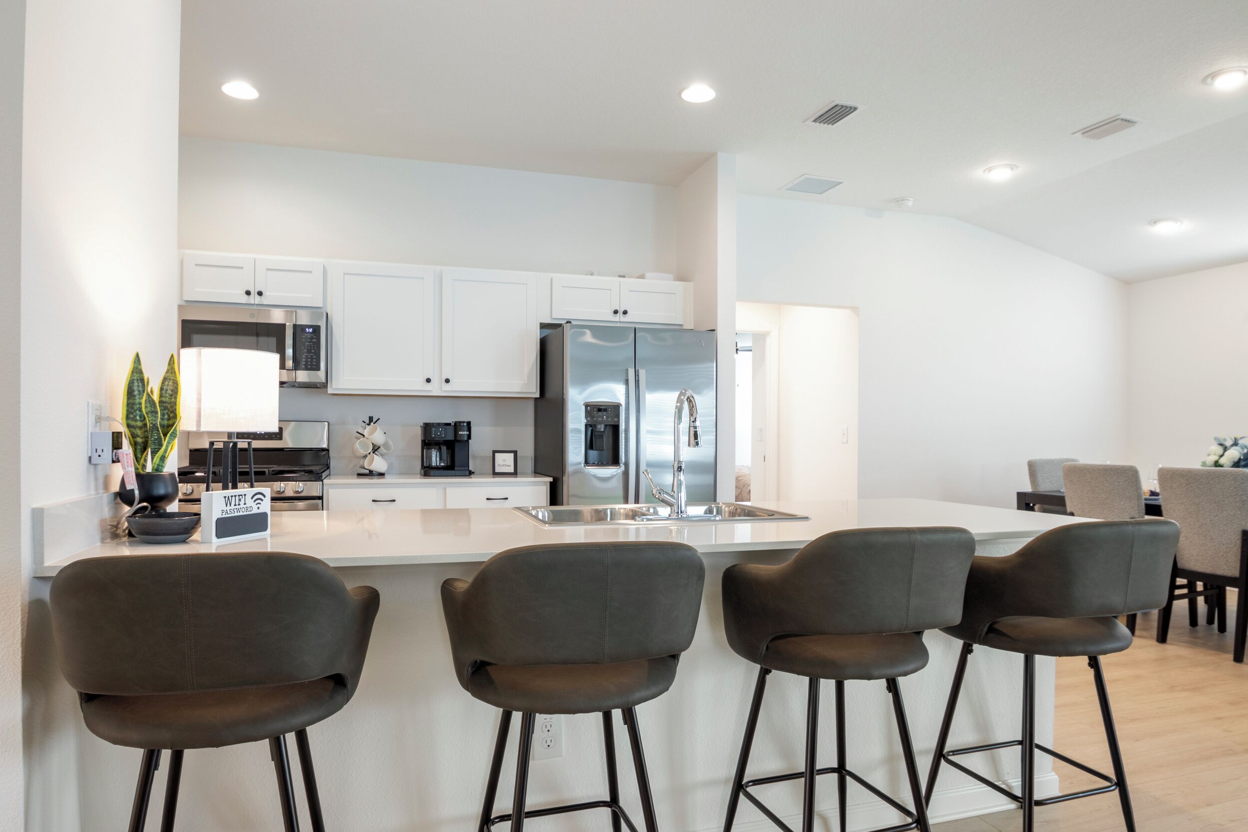 Una cocina moderna con armarios blancos, un refrigerador de acero inoxidable y una barra con taburetes.