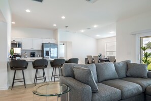 Una cocina moderna con armarios blancos, un refrigerador de acero inoxidable y una barra con taburetes.