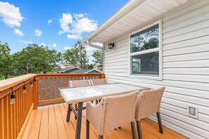 An outdoor deck with a glass-top table and wicker chairs, wooden railings, and a white exterior wall with a window. - Steps to Port of Kimberling & Table Rock Lake_Free Attraction Tickets (Kimberling City)