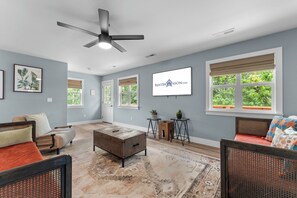 A spacious living room with a ceiling fan, a large window with a view of greenery, a mounted TV, and a cozy seating area with a sofa and a chair. - Steps to Port of Kimberling & Table Rock Lake_Free Attraction Tickets (Kimberling City)