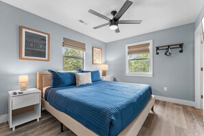 Ein Schlafzimmer mit Bett, Nachttischen, Deckenventilator und Fenstern mit Jalousien.