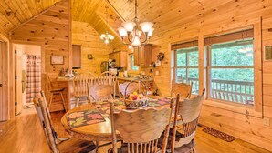 A wooden cabin interior with a dining area featuring a round table, chairs, and a chandelier.