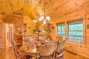 A wooden cabin interior with a dining area featuring a round table, chairs, and a chandelier.