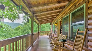 A wooden porch with rocking chairs and a table, overlooking a lush green landscape.