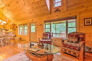 Ein Holzblockhaus-Interieur mit einem Glastisch, zwei gemusterten Sesseln und einem Essbereich mit Holzsesseln.