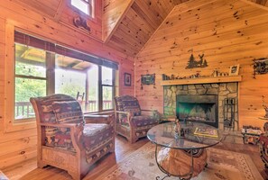 A cozy cabin interior with wooden walls, a stone fireplace, two patterned armchairs, and a glass coffee table.