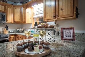 A kitchen with wooden cabinets, a granite countertop, a microwave, a wine bottle, and a sign that reads 'Welcome to our Cabin.' - Rosen Retreat | 3BR Cabin with hot tub, pool, game room, and fireplace (Helen)