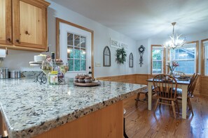 A kitchen with granite countertops, wooden cabinets, a dining area with a table and chairs, and a chandelier. - Rosen Retreat | 3BR Cabin with hot tub, pool, game room, and fireplace (Helen)