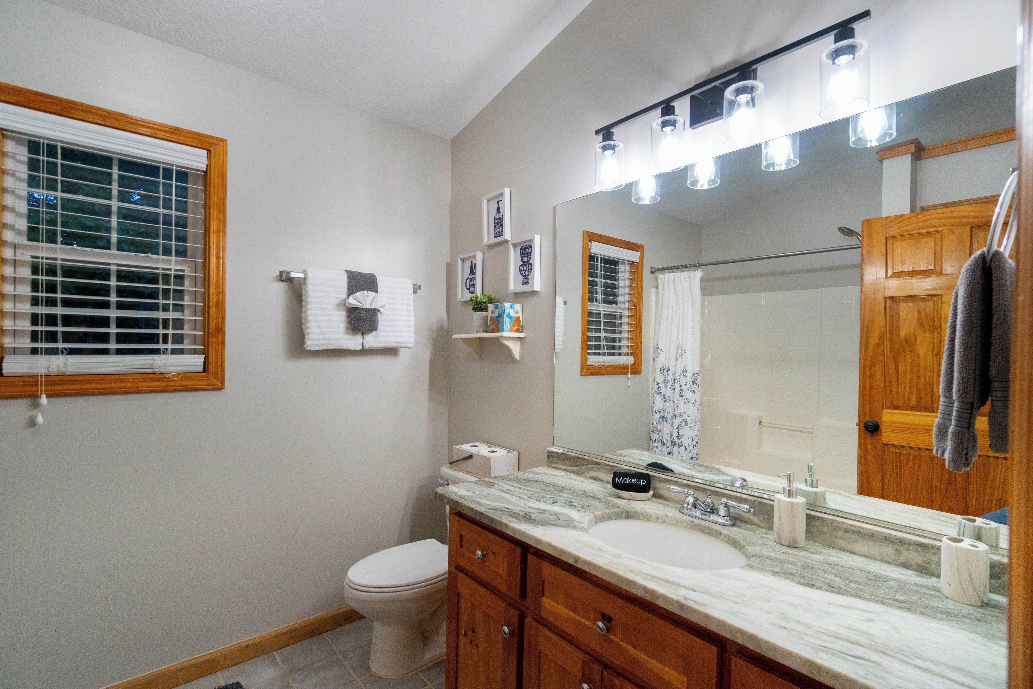 A bathroom with a toilet, sink, vanity, and a large mirror.