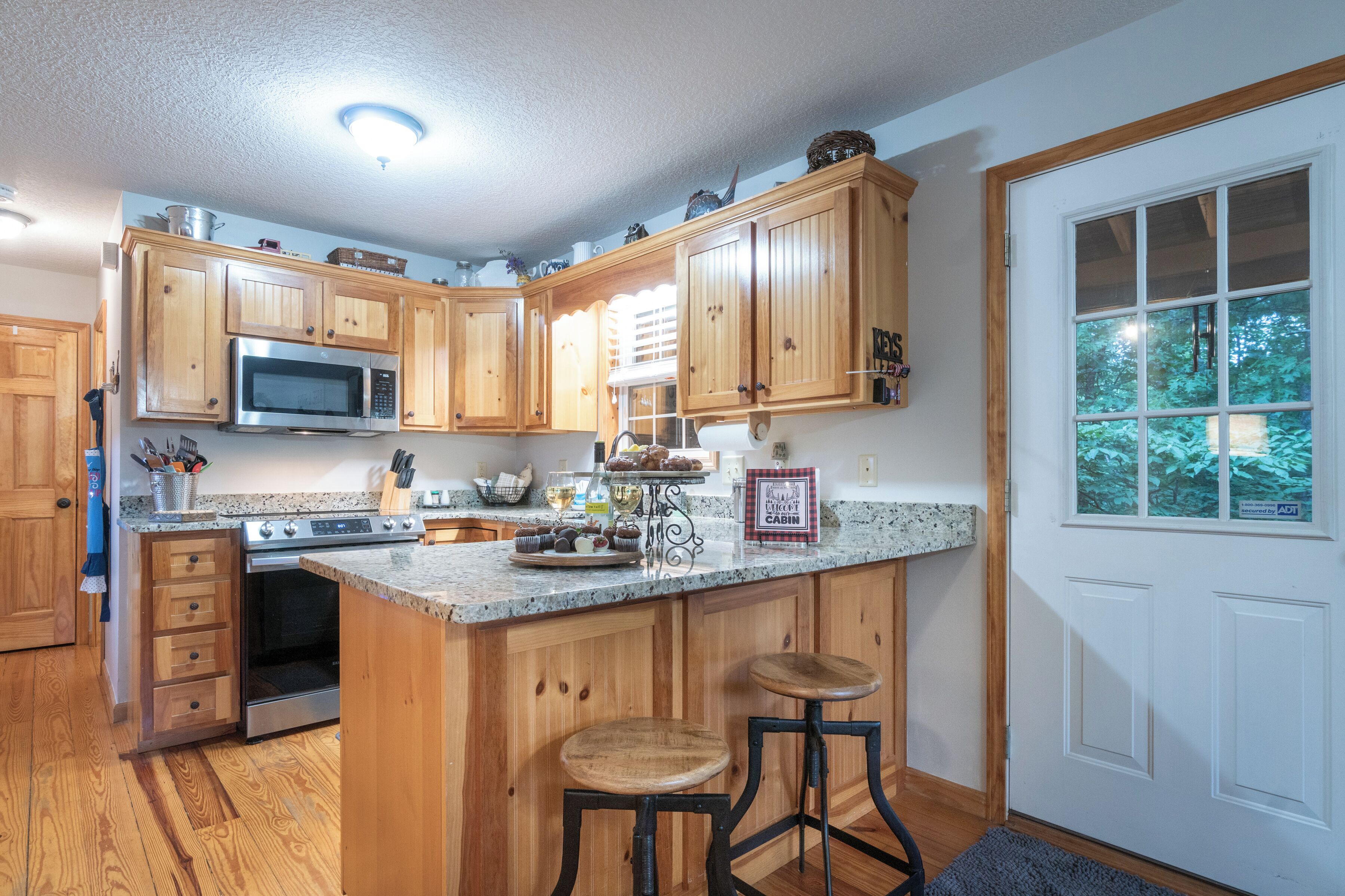 A kitchen with wooden cabinets, a microwave, an oven, and a large island with stools.