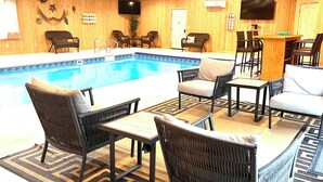 Un área de piscina con mobiliario de mimbre, un televisor y una pared de madera.