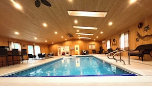 Una piscina interior con revestimiento de madera, rodeada de sillones de descanso y un ventilador de techo.