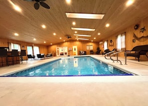 Una piscina interior con revestimiento de madera, rodeada de sillones de descanso y un ventilador de techo.