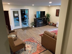 A living room with a sofa, a television, a fireplace, and a dining area visible through glass doors.