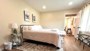 Un dormitorio con cama, una mesita de noche con lámpara, un tapete y dos cuadros en la pared.