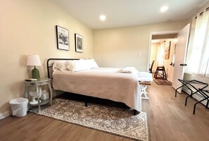 Un dormitorio con cama, una mesita de noche con lámpara, un tapete y dos cuadros en la pared.