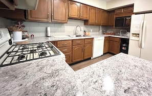 A kitchen with granite countertops, wooden cabinets, a gas stove, a dishwasher, and a refrigerator. - Private Indoor Heated Pool inside Spacious 4-bedroom house in serene Escanaba (Escanaba)