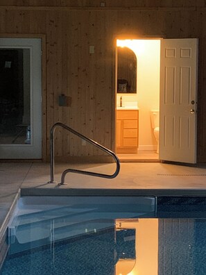 En swimmingpool med gelænder, en trædør og et badeværelse, der kan ses gennem en åben dør.
