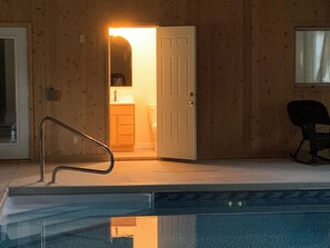 Een houten gevelwand, een deur naar een badkamer, een stoel en een zwembad.