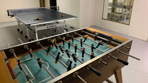 Ein Kicker und ein Tischtennis-Tisch in einem Raum mit Spiegel und Fenster.
