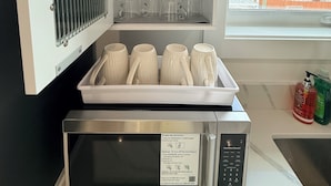 Cozinha com micro-ondas, armário de vidraria e janela com vista para edifícios.