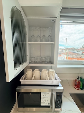 Una cucina con forno a microonde, un pensile per bicchieri e una finestra con vista sugli edifici.