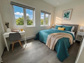 A bedroom with a bed, desk, chair, and windows.