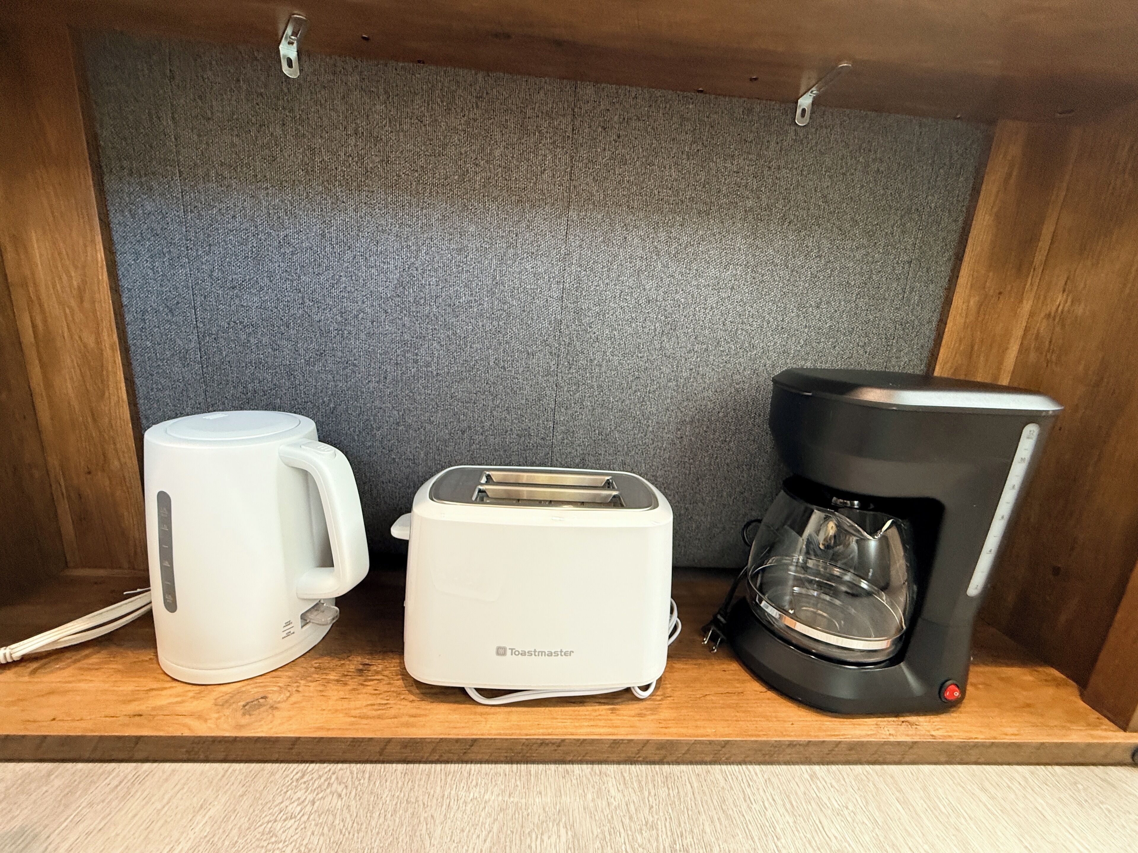 Une petite cuisine équipée d’un grille-pain, d’une machine à café et d’une tasse posée sur une étagère en bois.