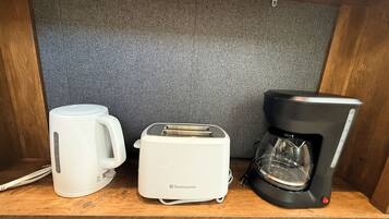 Une petite cuisine équipée d’un grille-pain, d’une machine à café et d’une tasse posée sur une étagère en bois.