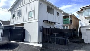Un edificio residencial de dos pisos con fachada blanca, una reja negra y una escalera visible que conduce a un nivel superior.