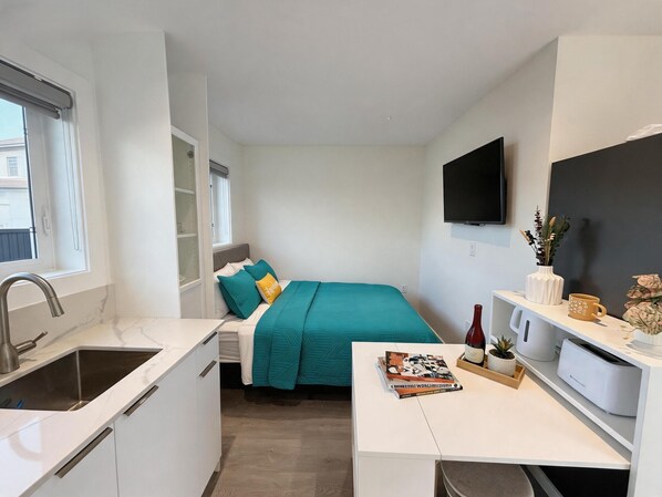 A compact room with a bed, a desk, a TV, and a window.