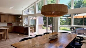 A modern kitchen with wooden cabinets, a large dining table, and a view of the outdoors through large windows. - Woodland - Stunning 5 bedroom home in GB! (Great Barrington)