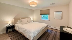 Ein Schlafzimmer mit Bett, Nachttischen, einer Lampe, einem Fenster mit Jalousien, einem Spiegel und einer Heizung.