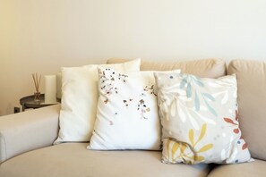 A beige sofa with three decorative pillows, a white candle, and a small table with a candle holder and reed diffuser. - Roots of Gaia by Hommelier (Vila Nova de Gaia)
