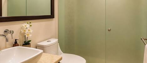 A bathroom with a large mirror, two sinks, a toilet, and a glass-enclosed shower.
