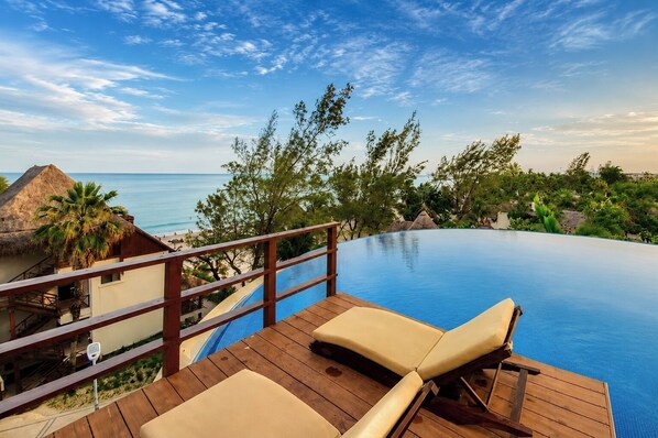 Eine Holzterrasse mit Pool, Liegestühlen und Blick auf Strand und Meer.