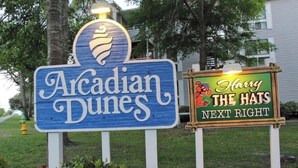 Een bord met 'Acadian Dunes' en een logo, en een ander bord voor 'Harry The Hats' dat een nabijgelegen locatie aangeeft.